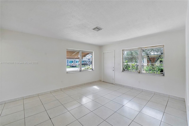 unfurnished room featuring light tile patterned floors, baseboards, visible vents, and a textured ceiling