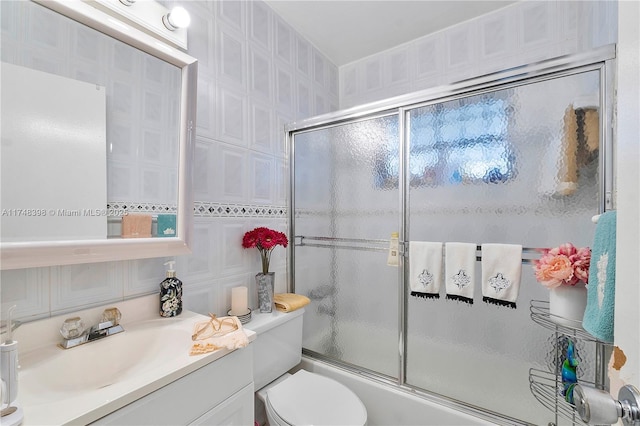 bathroom featuring toilet, enclosed tub / shower combo, tile walls, and vanity