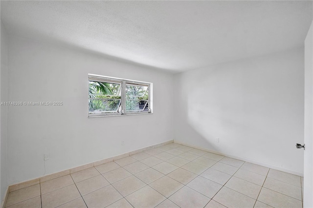 spare room featuring a textured ceiling, baseboards, and light tile patterned floors