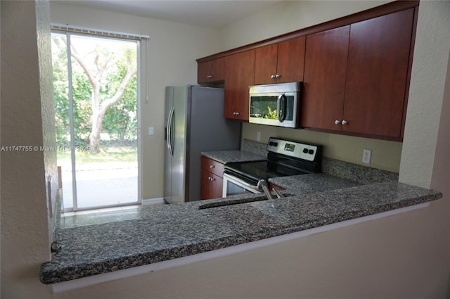 kitchen with sink, kitchen peninsula, appliances with stainless steel finishes, and dark stone countertops