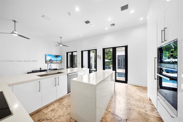 kitchen with appliances with stainless steel finishes, an island with sink, ceiling fan, sink, and white cabinetry