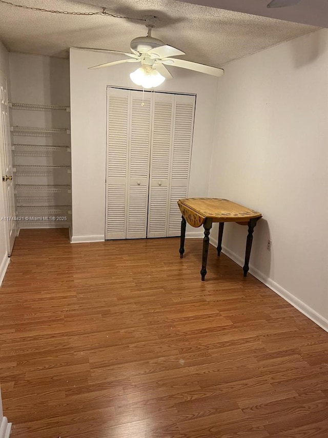 interior space featuring ceiling fan, a textured ceiling, baseboards, and wood finished floors