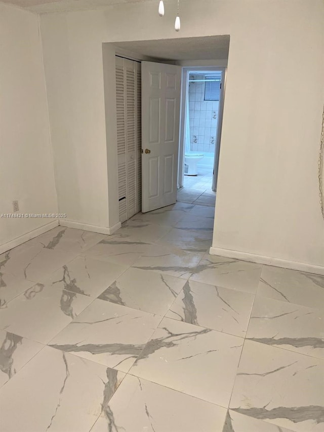 spare room featuring marble finish floor and baseboards