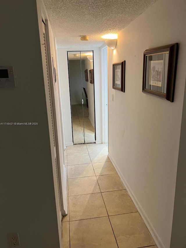 corridor featuring light tile patterned floors, a textured ceiling, and baseboards