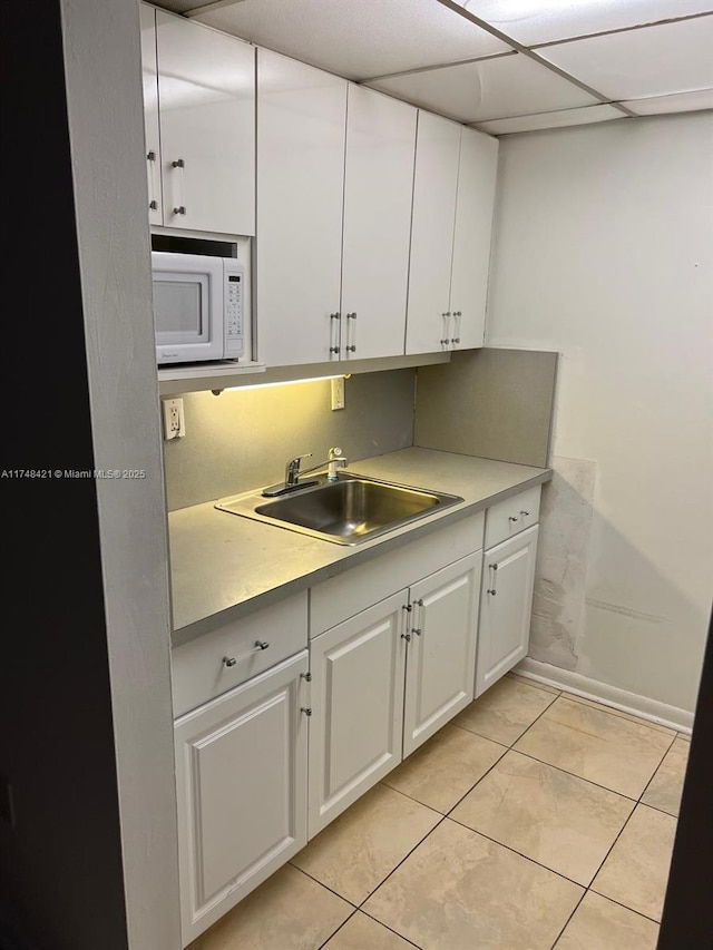 kitchen featuring white microwave, a drop ceiling, a sink, white cabinets, and light countertops