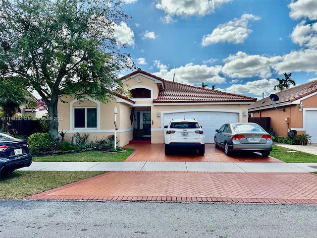 mediterranean / spanish-style home with decorative driveway, an attached garage, a tile roof, and stucco siding