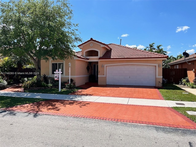 mediterranean / spanish home featuring a tile roof, stucco siding, fence, an attached garage, and decorative driveway