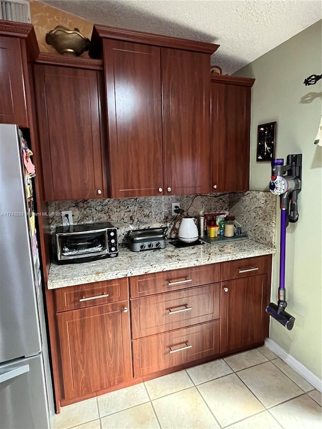 kitchen featuring light tile patterned flooring, light stone counters, backsplash, freestanding refrigerator, and a textured ceiling