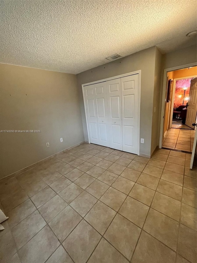 unfurnished bedroom featuring light tile patterned flooring, visible vents, a closet, and a textured ceiling