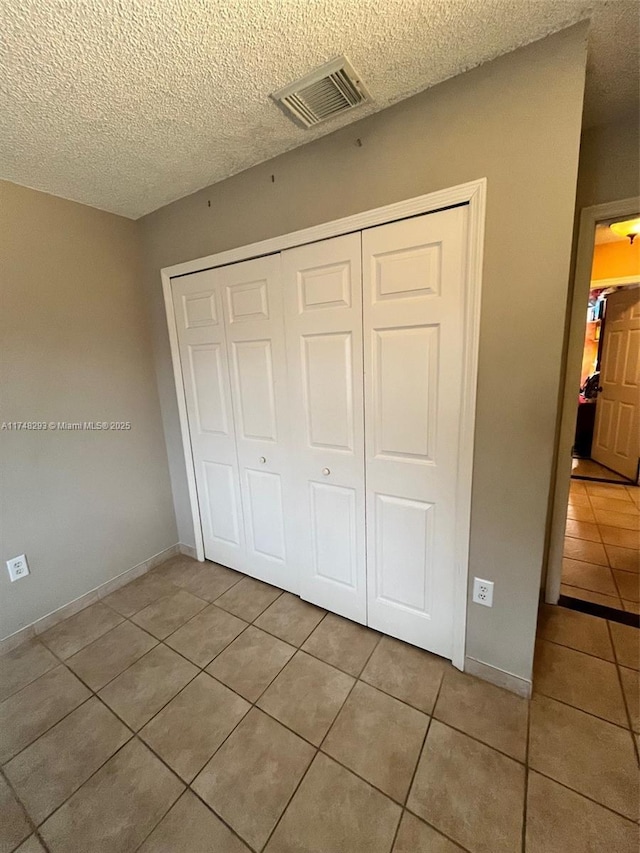 unfurnished bedroom featuring a textured ceiling, visible vents, a closet, and light tile patterned floors