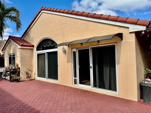 back of house featuring stucco siding, a tiled roof, and a patio