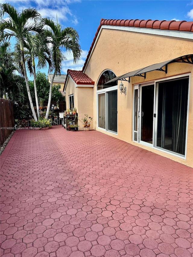 back of house with stucco siding, a tile roof, fence, and a patio