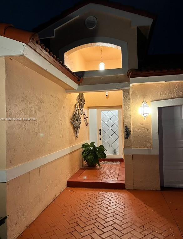 hallway featuring a raised ceiling, a textured wall, and brick floor