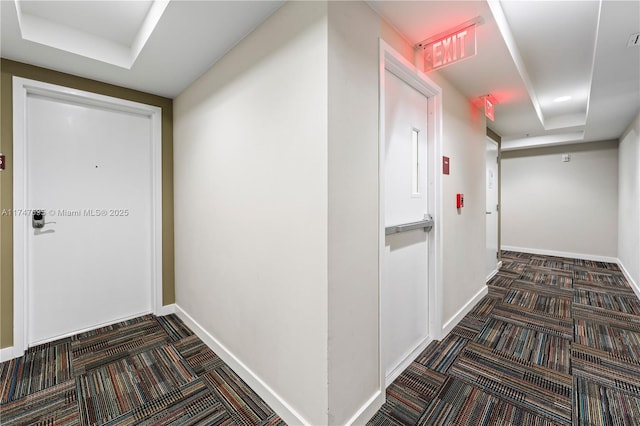 hallway featuring dark colored carpet and a raised ceiling