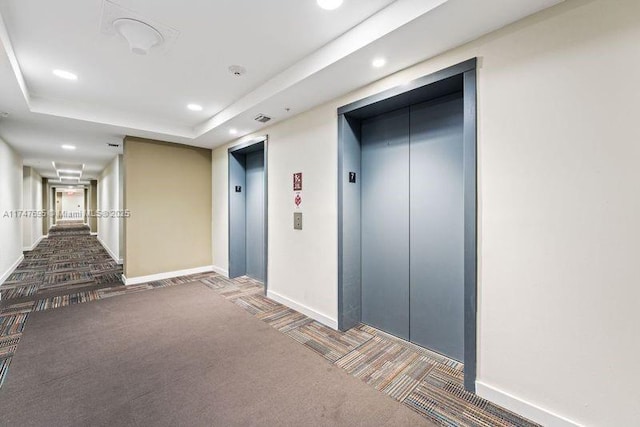 hallway featuring a raised ceiling, elevator, and dark colored carpet