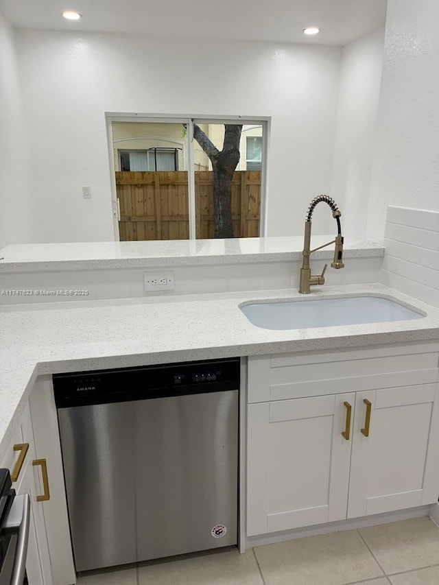 kitchen with light stone countertops, white cabinets, stainless steel dishwasher, light tile patterned floors, and sink