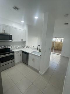 kitchen featuring white cabinetry, stainless steel appliances, light tile patterned floors, and sink