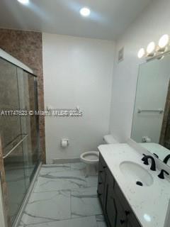 bathroom featuring toilet, an enclosed shower, and vanity