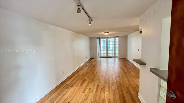 unfurnished living room with rail lighting, baseboards, light wood-style floors, and expansive windows