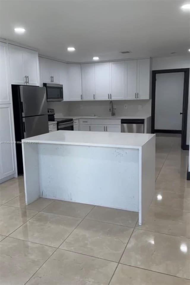 kitchen with light countertops, appliances with stainless steel finishes, white cabinetry, a sink, and a kitchen island