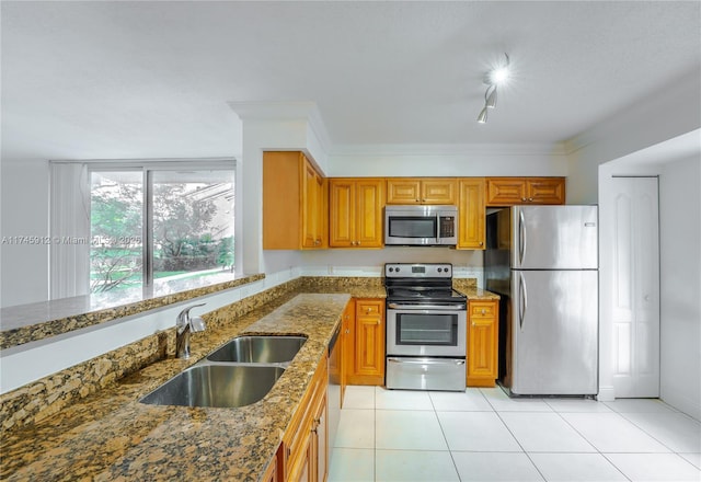 kitchen featuring a sink, appliances with stainless steel finishes, brown cabinetry, stone counters, and light tile patterned flooring
