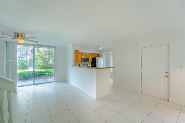 kitchen with light tile patterned floors, appliances with stainless steel finishes, a ceiling fan, a peninsula, and brown cabinets