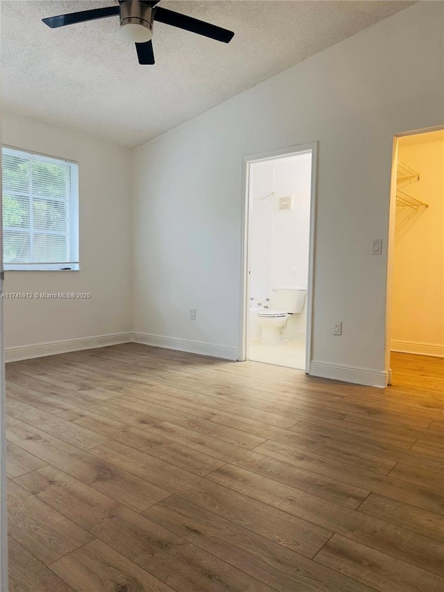 unfurnished bedroom featuring a closet, a spacious closet, hardwood / wood-style flooring, a textured ceiling, and connected bathroom
