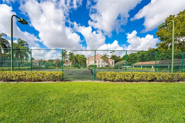 view of community featuring a tennis court, a yard, and fence