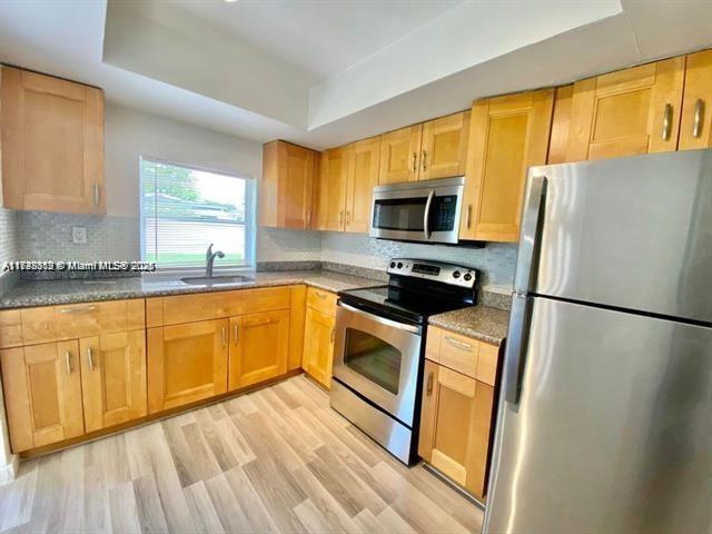 kitchen featuring light hardwood / wood-style flooring, sink, a tray ceiling, tasteful backsplash, and appliances with stainless steel finishes