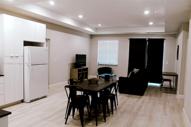 dining room with light wood-type flooring and a raised ceiling