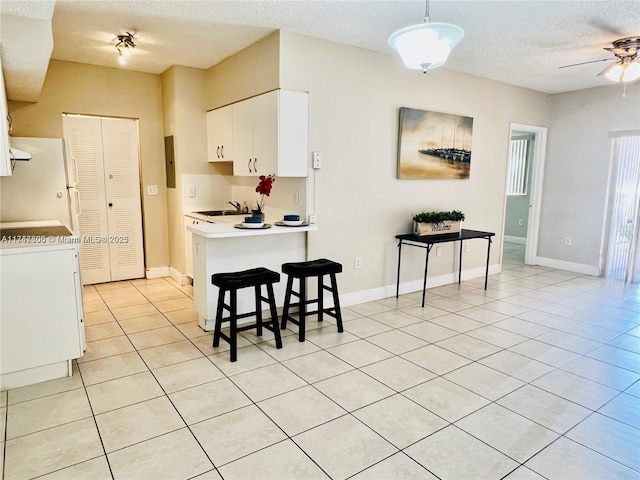 kitchen with a sink, light tile patterned flooring, freestanding refrigerator, a textured ceiling, and white cabinetry