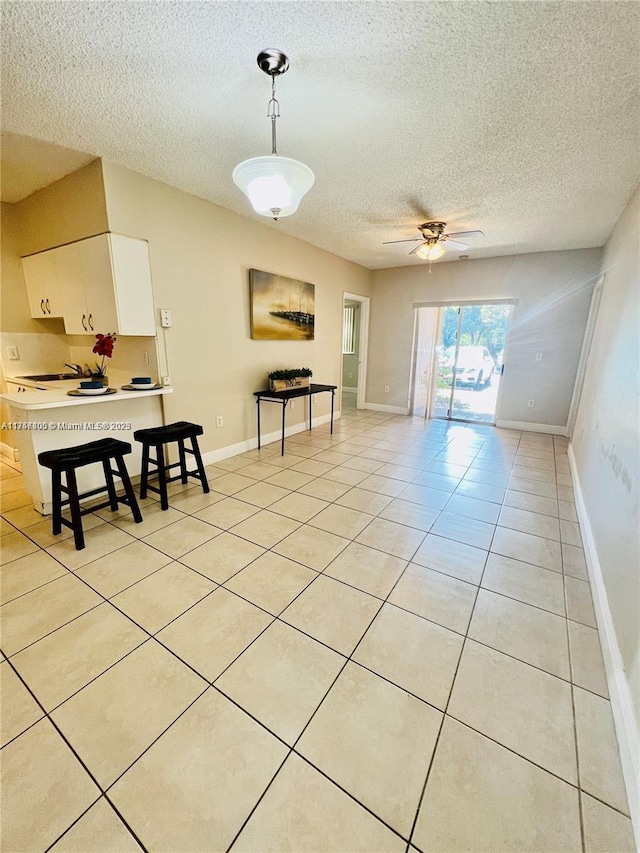 living area featuring a ceiling fan, baseboards, light tile patterned flooring, and a textured ceiling