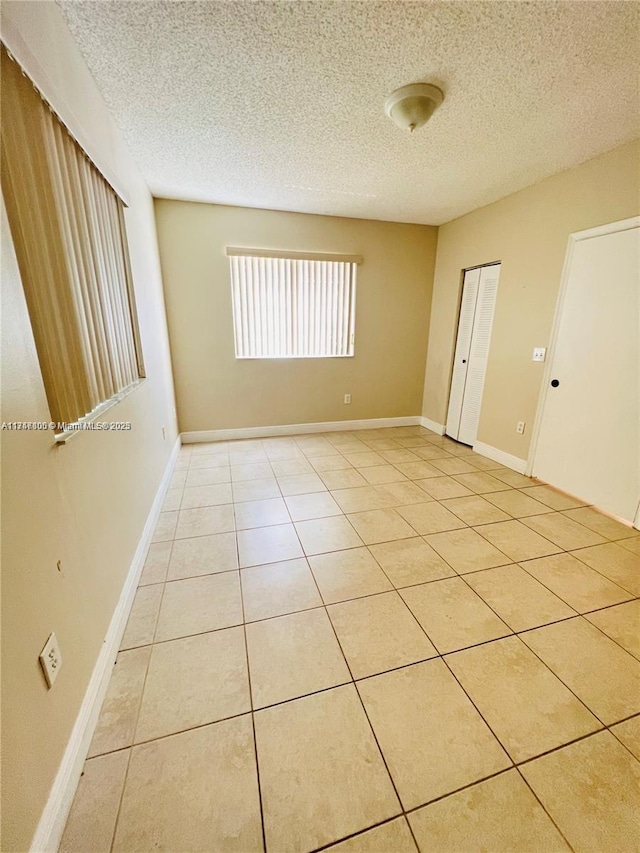 empty room featuring baseboards, light tile patterned flooring, and a textured ceiling