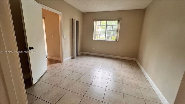 empty room with baseboards, a textured ceiling, and light tile patterned floors