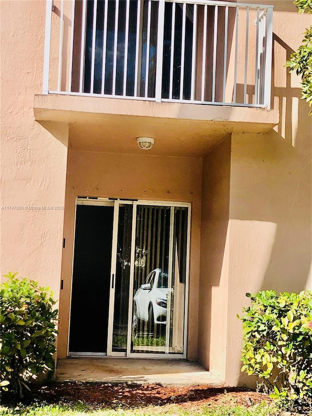 view of exterior entry with a balcony and stucco siding