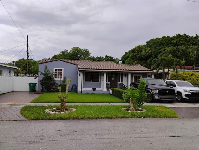 view of front facade with driveway, a tile roof, fence, a front yard, and stucco siding