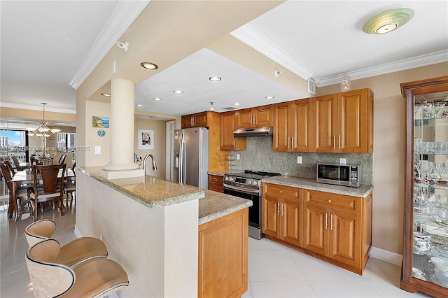 kitchen with appliances with stainless steel finishes, light stone countertops, decorative light fixtures, a breakfast bar, and ornate columns