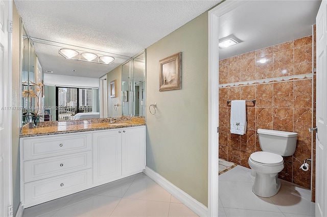 bathroom with tile patterned floors, toilet, tile walls, a textured ceiling, and vanity