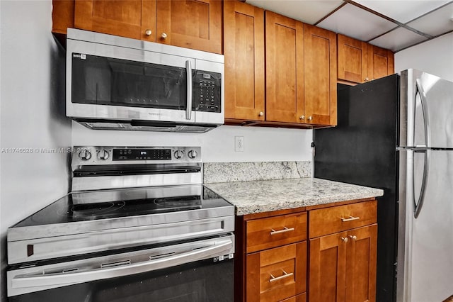 kitchen featuring brown cabinetry, light stone counters, stainless steel appliances, and a drop ceiling