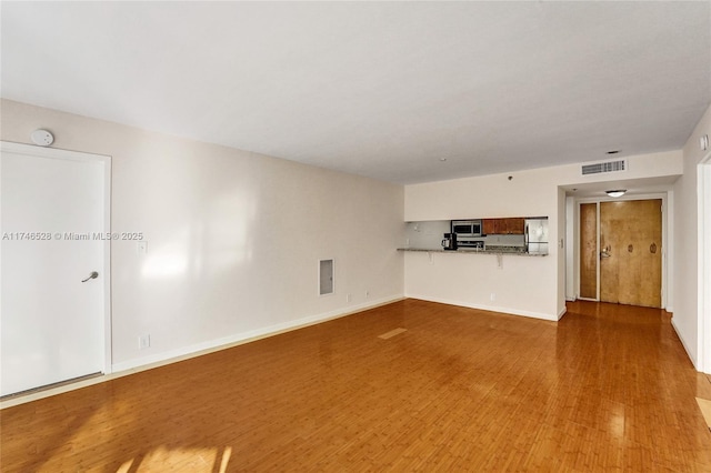 unfurnished living room featuring wood finished floors, visible vents, and baseboards