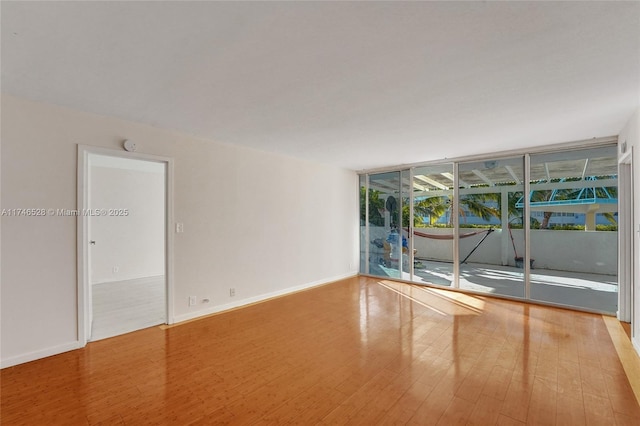 unfurnished room featuring expansive windows, baseboards, and wood finished floors