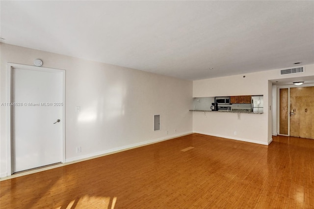 unfurnished living room featuring baseboards, visible vents, and wood finished floors