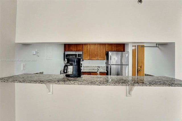 kitchen with a peninsula, appliances with stainless steel finishes, a breakfast bar, and brown cabinets