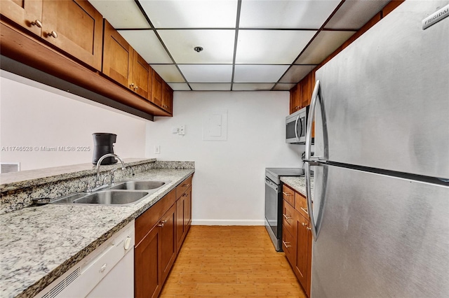 kitchen with stainless steel appliances, light hardwood / wood-style flooring, light stone countertops, sink, and a drop ceiling