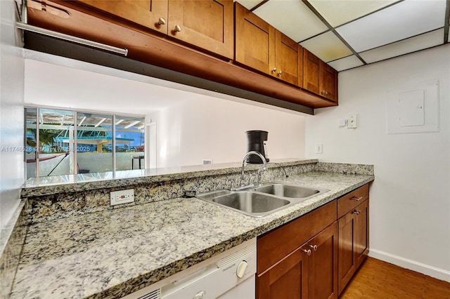 kitchen featuring light stone counters, a drop ceiling, a sink, baseboards, and light wood-style floors
