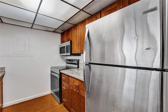 kitchen with light wood finished floors, appliances with stainless steel finishes, brown cabinetry, and a drop ceiling