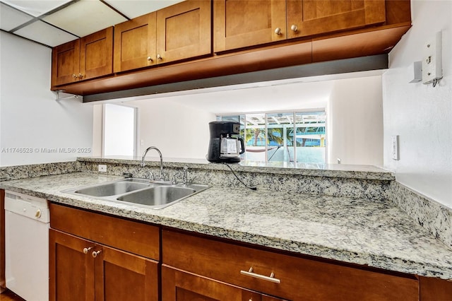 kitchen with a sink, light stone counters, brown cabinets, and dishwasher