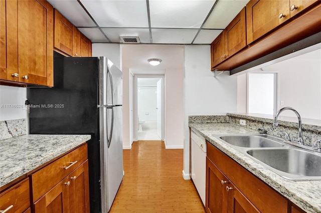 kitchen with a sink, freestanding refrigerator, light stone countertops, dishwasher, and brown cabinetry