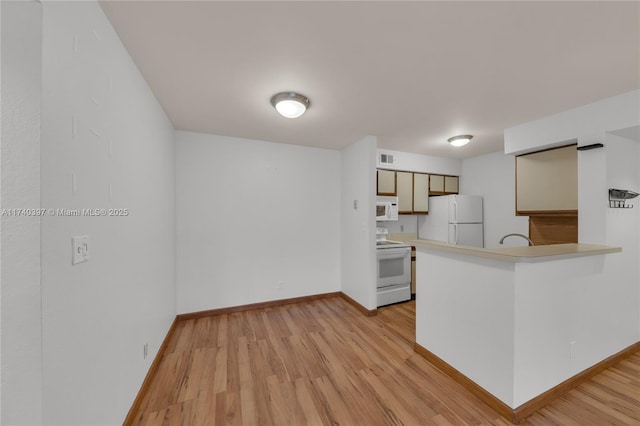 kitchen featuring light wood finished floors, light countertops, white appliances, a peninsula, and baseboards