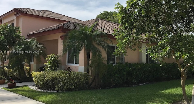 view of side of property featuring a tiled roof, a yard, and stucco siding